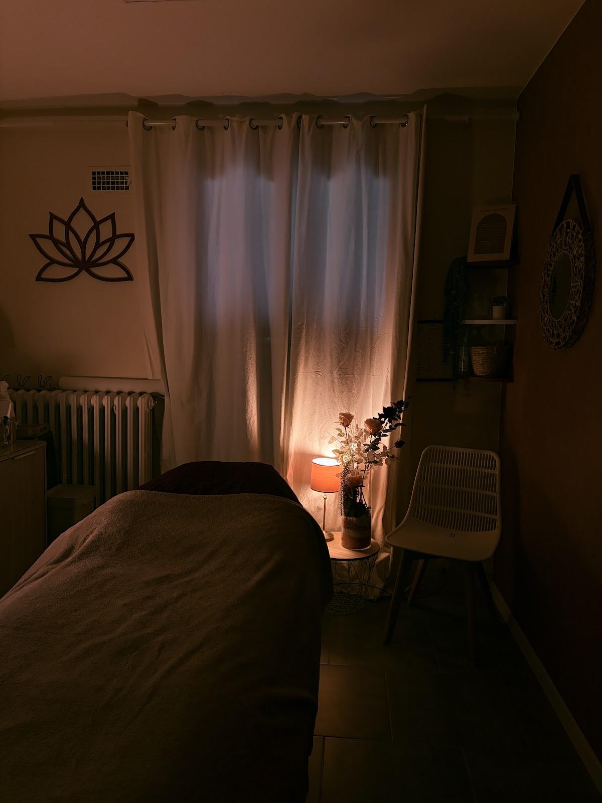 La cabine de soins, lumière tamisée : une table de soin, une lampe allumée, un lotus au mur.